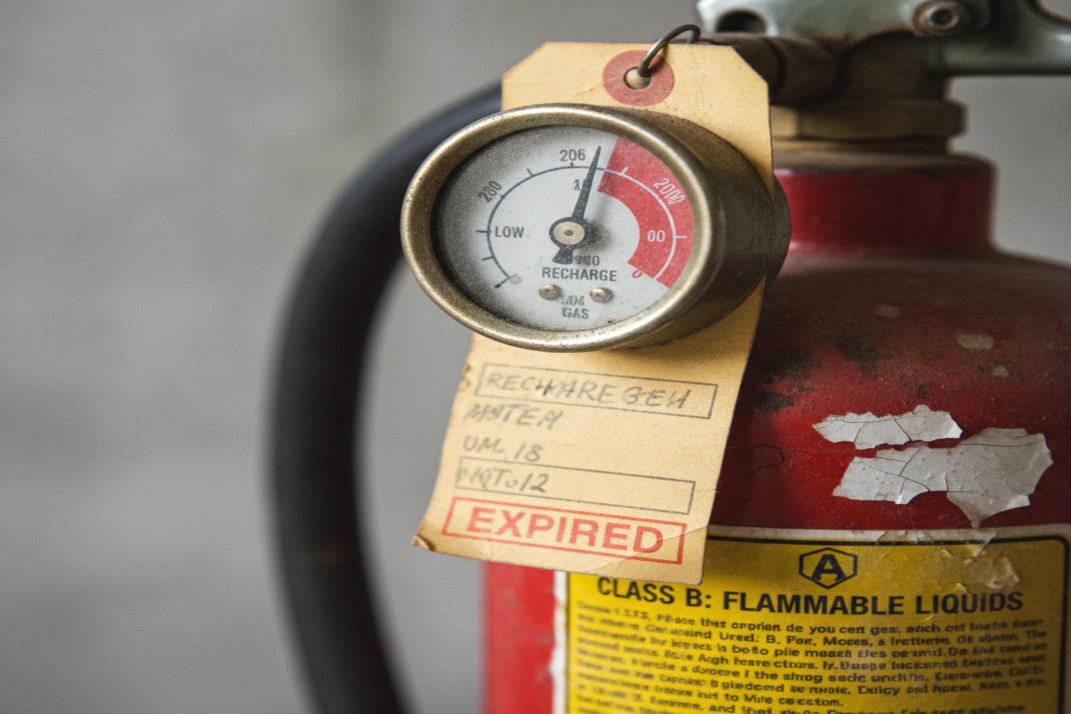 Comparison of old expired fire extinguisher next to a new replacement unit showing the manufacturing date and inspection tag